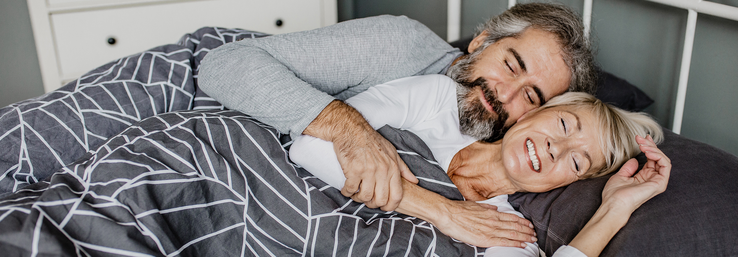 Older couple smiling, laying in bed